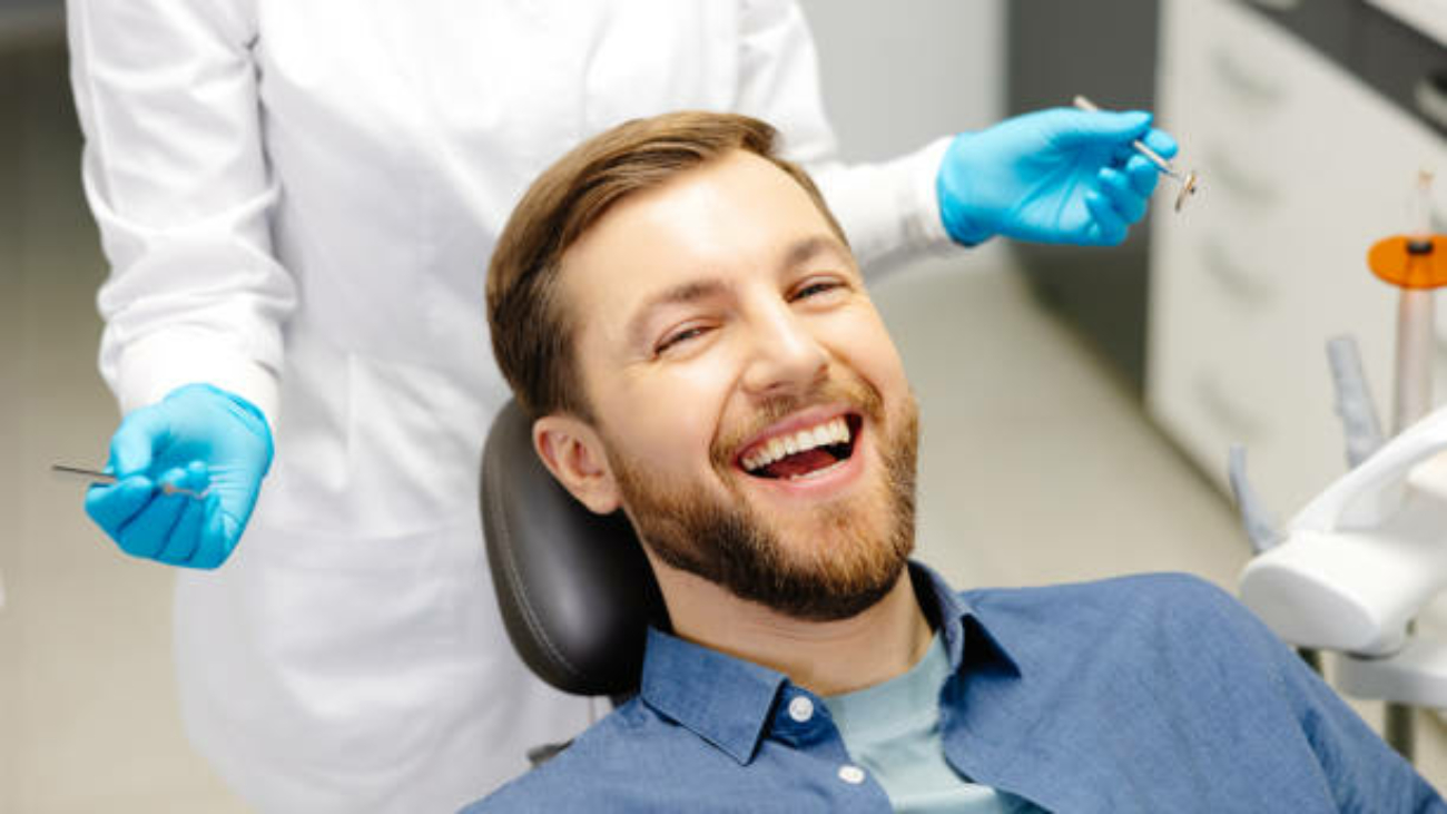 Portrait of happy man sitting at dentist chair in modern clinic and smiling. Patient enjoying dental treatment with professional dentist.