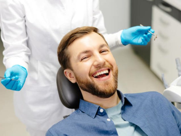 Portrait of happy man sitting at dentist chair in modern clinic and smiling. Patient enjoying dental treatment with professional dentist.