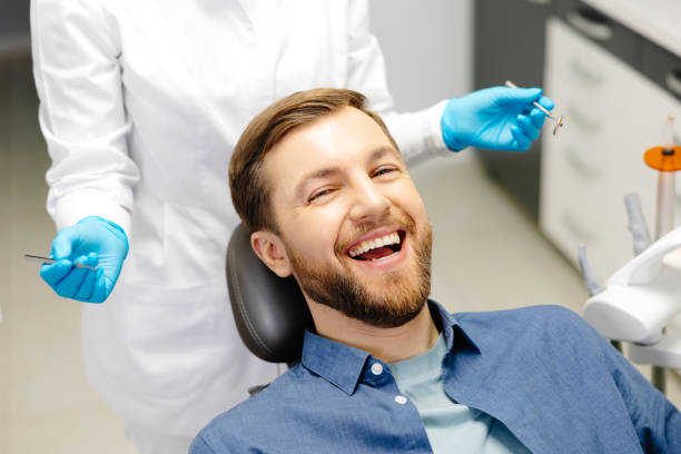 Portrait of happy man sitting at dentist chair in modern clinic and smiling. Patient enjoying dental treatment with professional dentist.