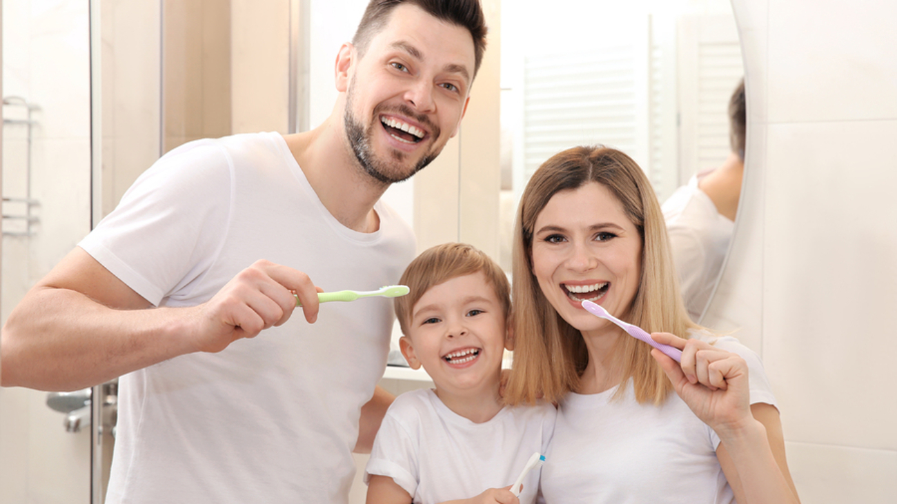Young couple and their beautiful son brushing teeth near mirror in bathroom