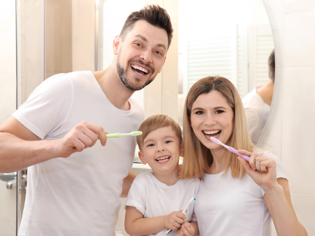 Young couple and their beautiful son brushing teeth near mirror in bathroom