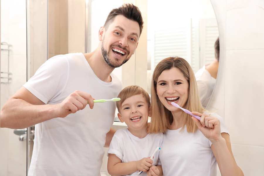 Young couple and their beautiful son brushing teeth near mirror in bathroom